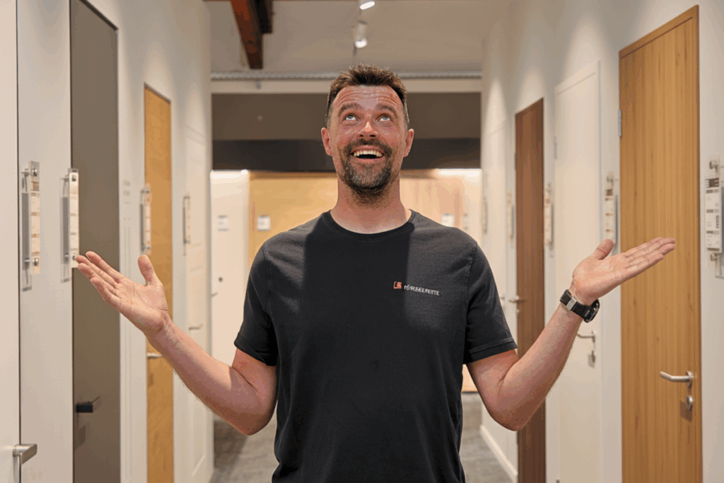 Türenexperte Roland Kruse steht in einer modernen Ausstellung zwischen verschiedenen Innentüren und blickt begeistert nach oben. Beratung zu flächenbündigen und wandbündigen Türen in der Fachausstellung.