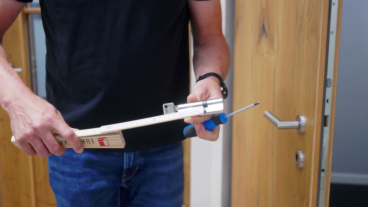 Ausgebauter Schließzylinder wird mit einem Zollstock ausgemessen, Nahaufnahme in der Hand